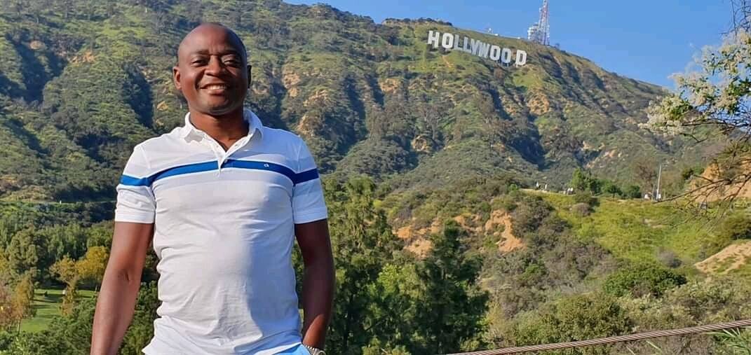 Hamis Kiggundu stands next to Hollywood sign in the USA